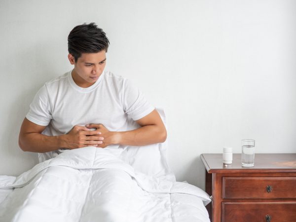 A man sits in bed with a stomachache and presses his stomach wit A man sits in bed with a stomachache and presses his stomach with his hands.